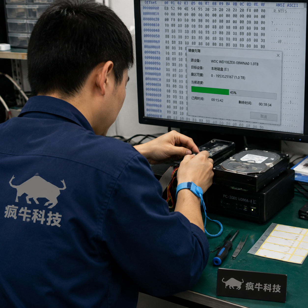 手机纪实抓拍，镜头聚焦在数据恢复工作台上。一台3.5寸机械硬盘正通过排线连接到专业的数据恢复设备上，背景的电脑屏幕上显示着十六进制代码和镜像克隆进度条。一位东亚技术员的手正在调整接线，他手腕上戴着防静电手环，身穿带有“疯牛科技”标志的蓝色工作服。桌面上有螺丝刀和标签纸，光线自然，充满真实的数码维修铺氛围。