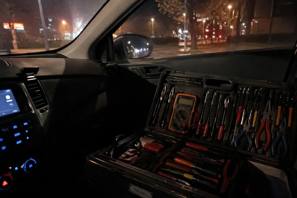 纪实抓拍。深夜的汽车副驾驶位上,放着一个打开的专业精密维修箱,里面整齐排列着万用表和工具。车窗外是郑州深夜模糊的街景,仪表盘的微光照亮了工具箱的一角,光影自然,像是由博主随手记录的工作瞬间。